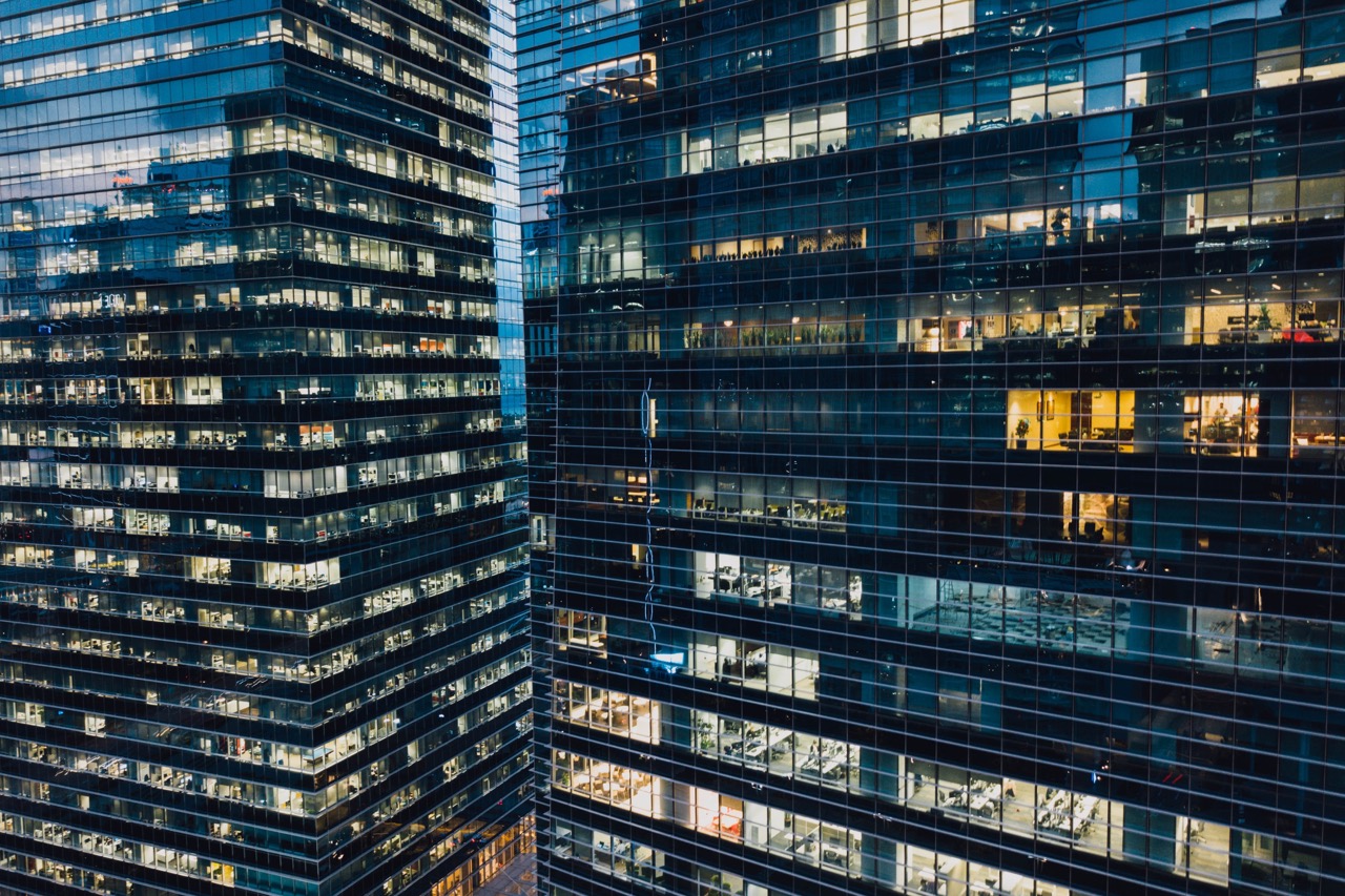 Two office buildings with lights on inside, photo by CHUTTERSNAP on Unsplash